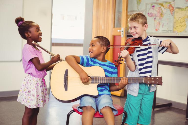 Three smiling children playing the guitar, violin, flute in a classroom at school