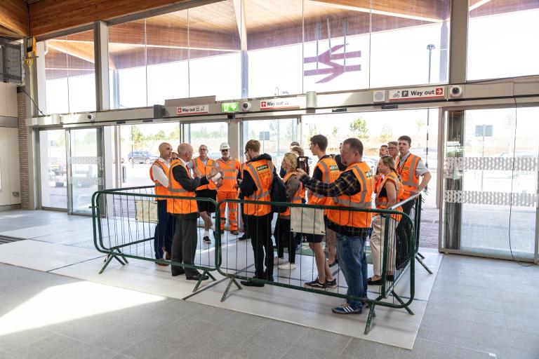 Group of people in hi-vis in a train station terminal behind barriers.