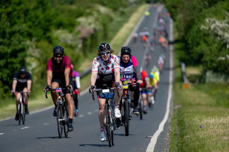 cyclists ride down a rural Essex road, smiling at the camera