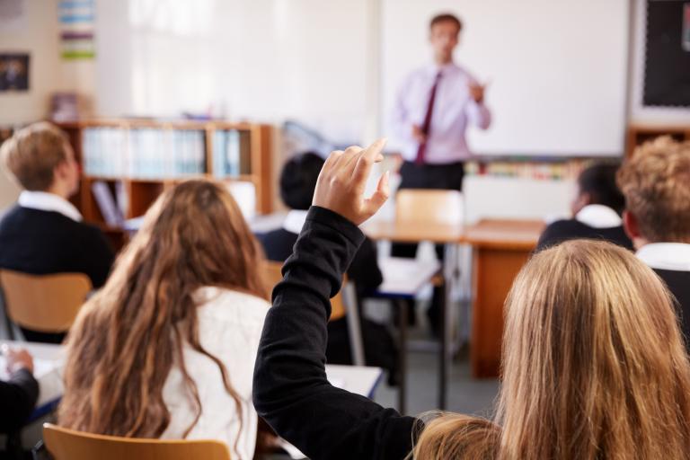 A photo inside a classroom, with a teacher at the front and pupils behind. 