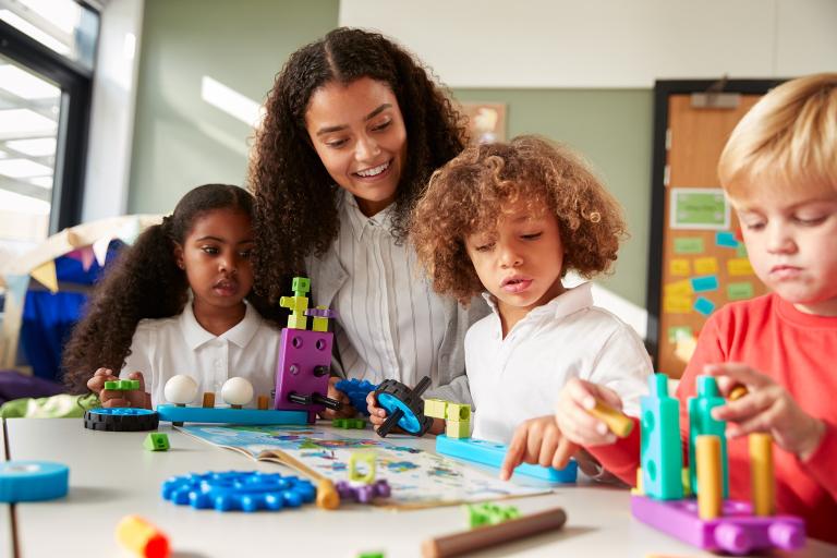 Female early years practitioner sitting at a table with three young children