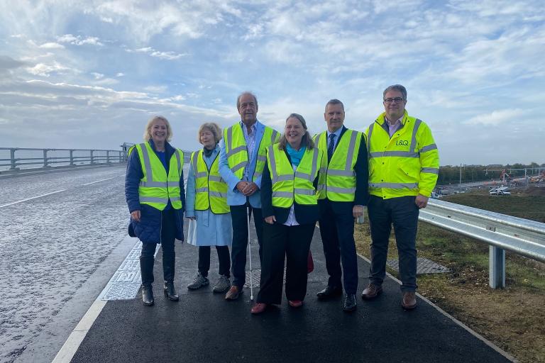 Six people wearing yellow high-visibility jackets standing on the newly opened bridge.