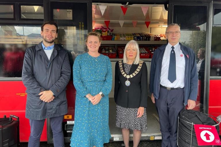 Four people standing outside the new community supermarket, which is a double decker bus.