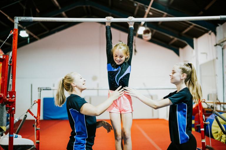 Young gymnast on a bar being supported by older children