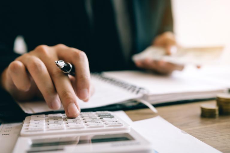 A close up shot of a person using a calculator whilst holding a pen. 