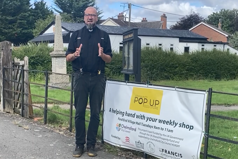 A person stands in front of a banner for Ford End community supermarket