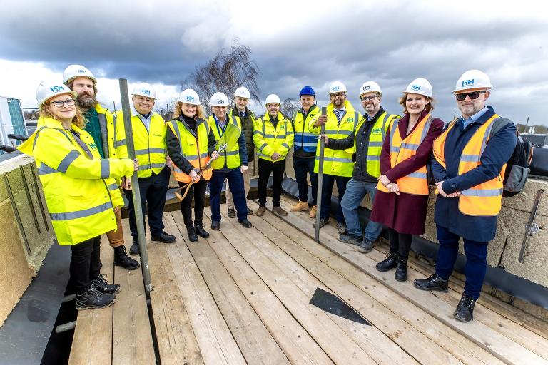 A group of people standing in a semi-circle wearing high-visibility jackets and hard hats on a building site.