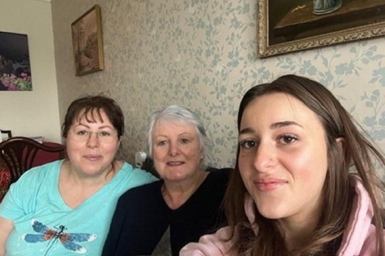 Three women sitting on a sofa smiling at the camera.