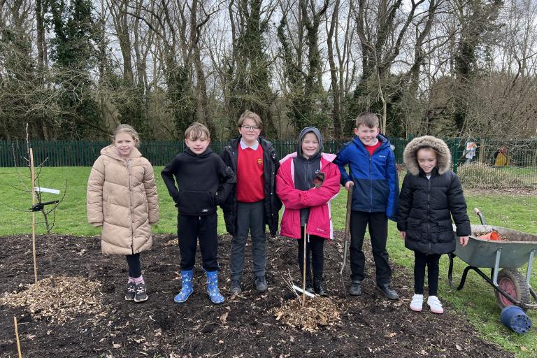 Schoolchildren in a row with shovels outside on an overcast day.