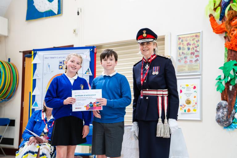 Lord Lieutenant in ceremonial uniform with students from Holy Trinity holding a certificate.