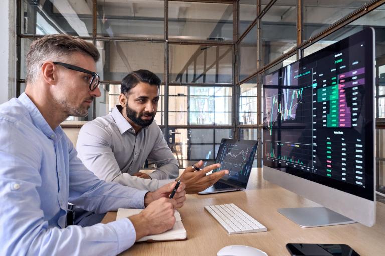 Two men sitting looking at figures on a computer.