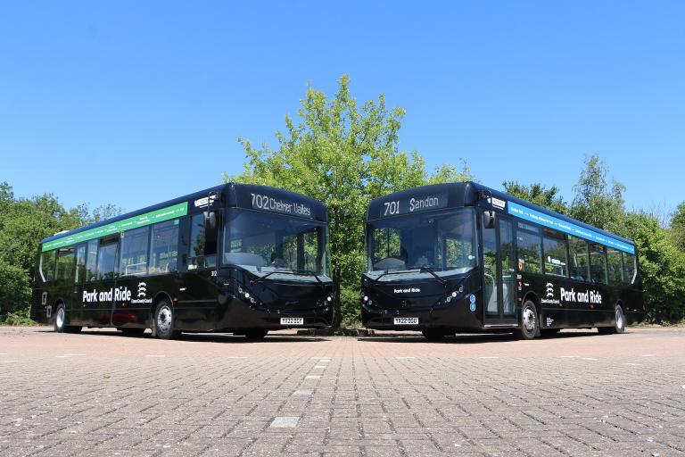 Busses face each other while parked side-by-side in the distance against blue skie.