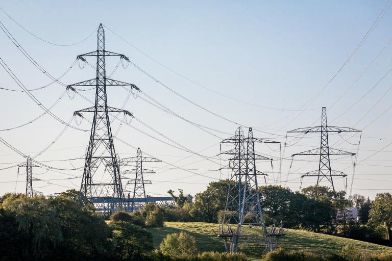 Pylons loom over a rural backdrop under dusky blue skies.