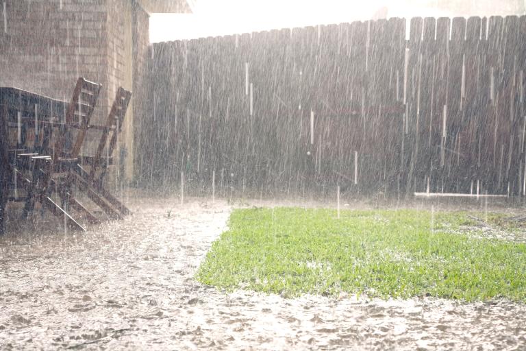 Heavy rainfall in a garden showing garden furniture, path and grass. Water is unable to soak into the ground.