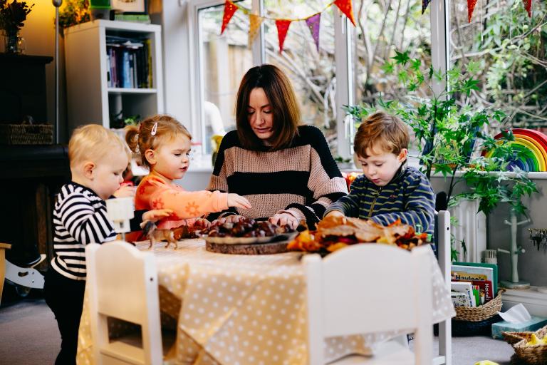 Three young children and a woman sitting around a table with craft items in front of them.