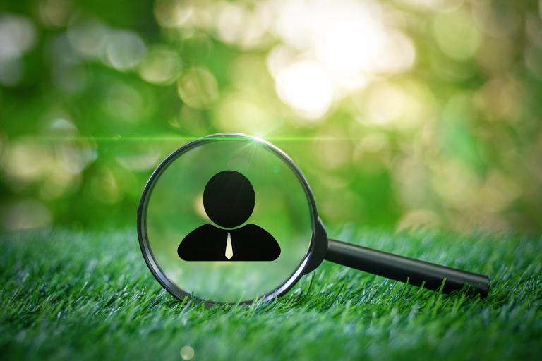 Magnifying glass against green grass with silhouette of businessman printed onto lens.