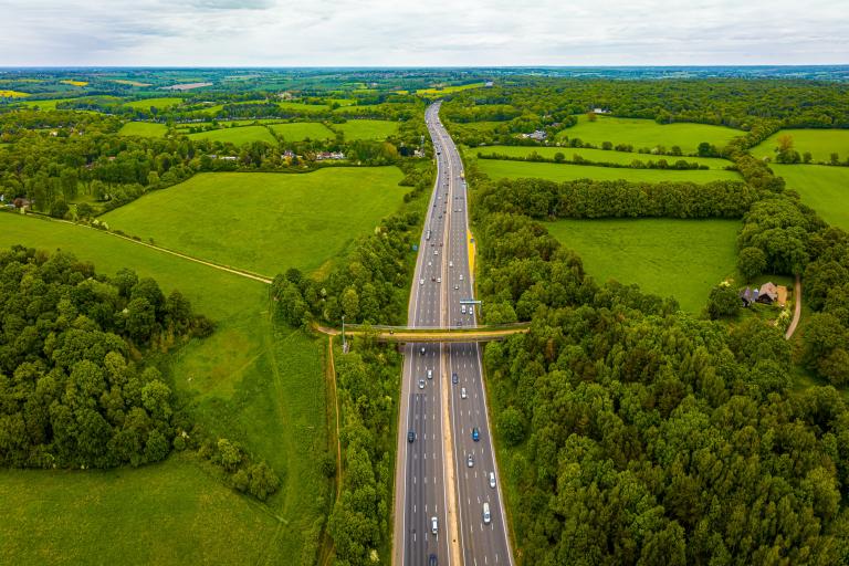 Aerial shot of straight highway cutting through green hills and trees.