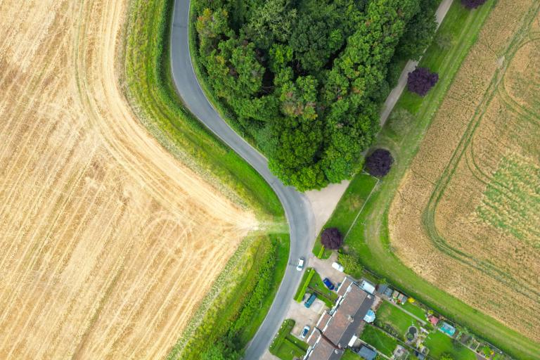 Bird's-eye view of road snaking past fields and a small village.