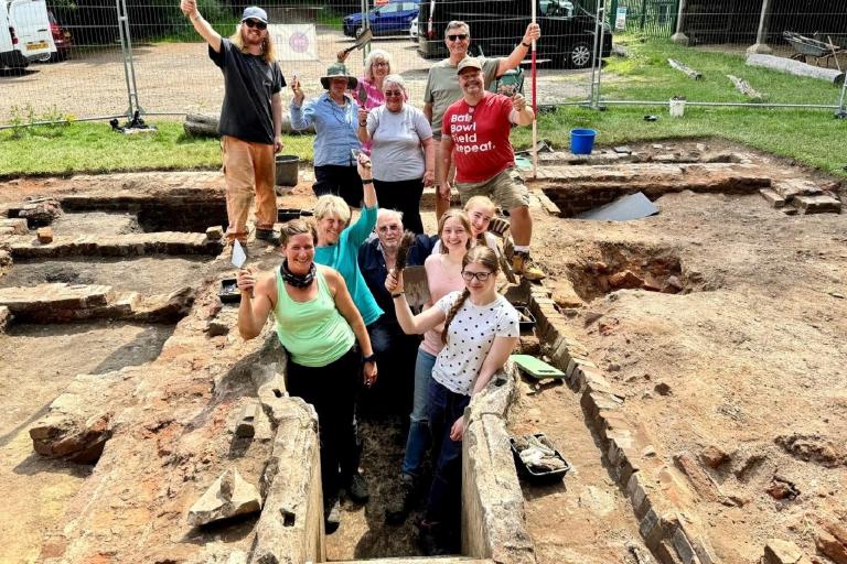 A large group of people huddled around an excavated bath structure on an archaeological site