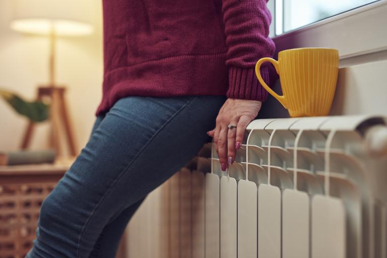 Woman in jumper leans back against radiator.