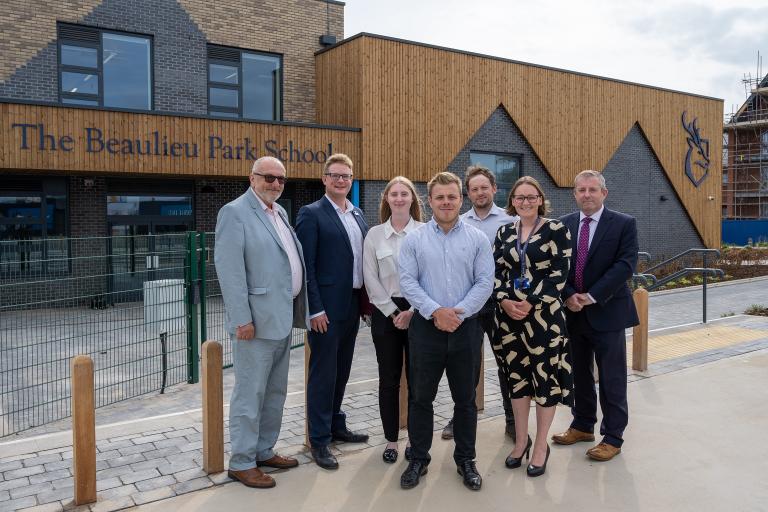 Six people standing outside a modern building, with a sign saying "The Beaulieu Park School". Picture credit - RG Carter