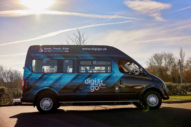 A man sits at the steering wheel of a black DigiGo branded mini bus.