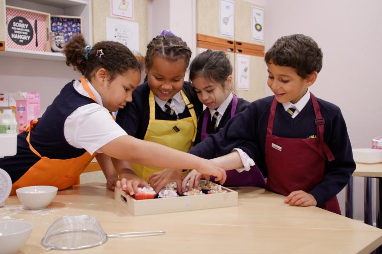 Four young children baking in the kitchen with aprons on.