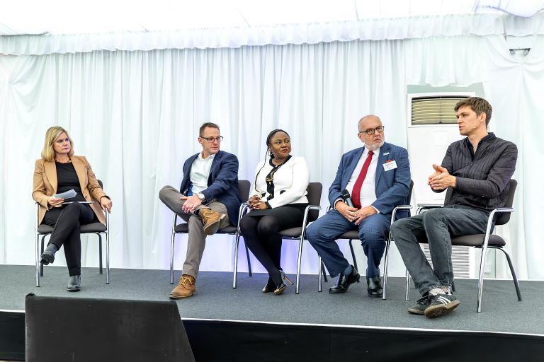 Five panel members sitting on chairs on a stage. 