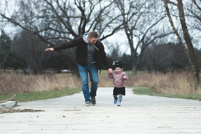 Man holding hands with a little girl, running along a boardwalk