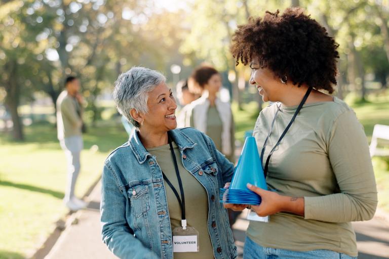 Two women smile and embrace in a sunny park.