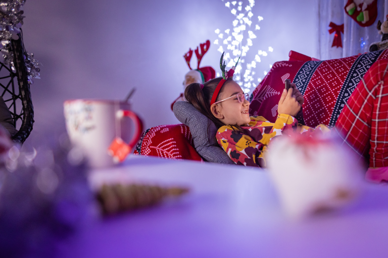 Young child on the sofa on her mobile phone with christmas decorations across the room.