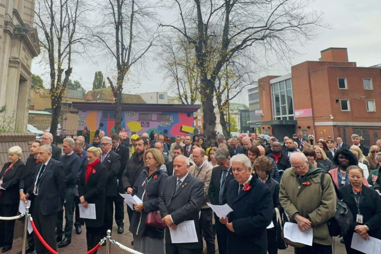 Huddle of men and women in black winter coats observe a minute's silence at a service in County Hall, Chelmsford.