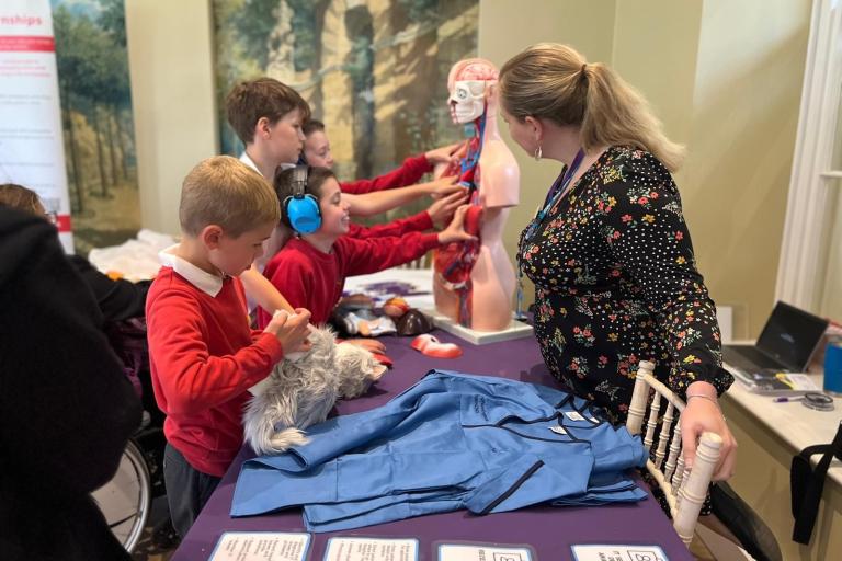 Four male pupils interacting with a medical model of the human body at an event stall while a member of staff looks on.