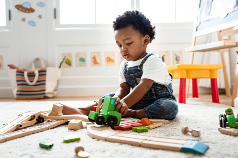 Little boy playing with wooden railroad train toy on the floor.