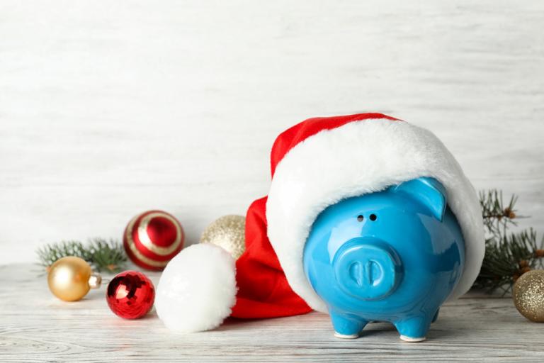 Blue piggy bank wearing a red santa hat and surrounded by red and silver baubles.