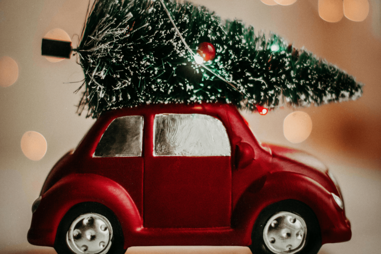 Red metallic car figurine, with a green Christmas tree tied to the roof.