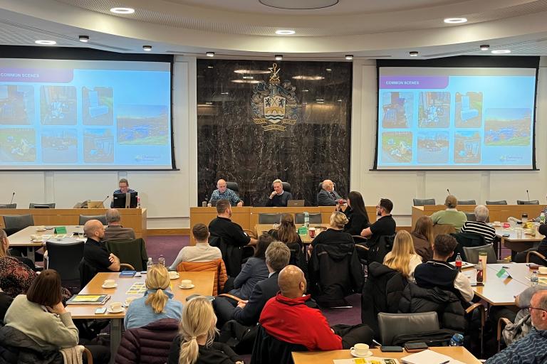 Chelmsford council chambers with several busy roundtables facing large screens.