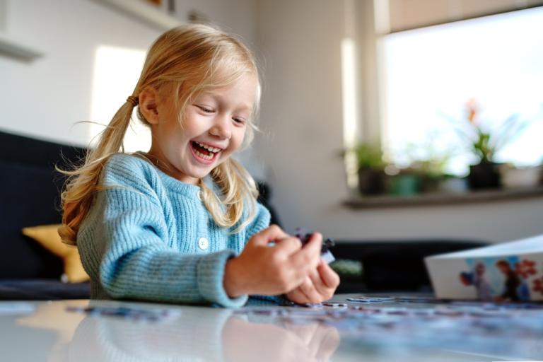 Young girl smiling playing with a jigsaw puzzle at the table 