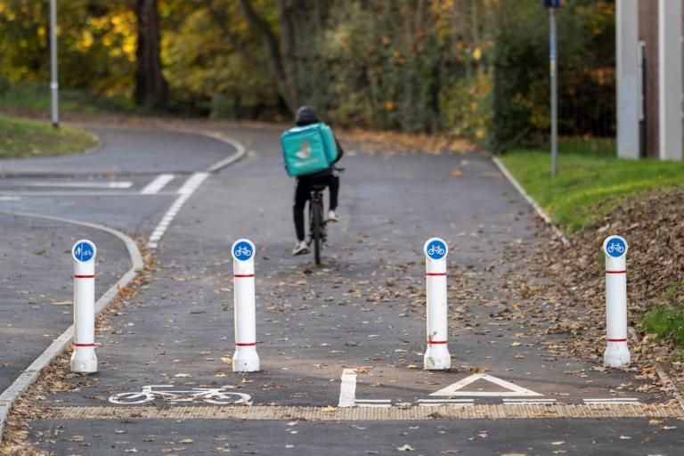 Cyclist rides away in the distance beyond cycling bollards.