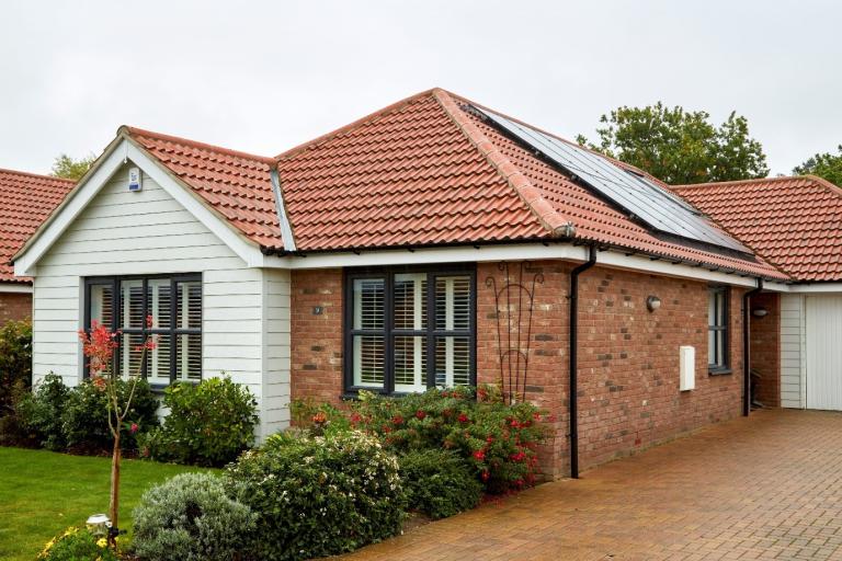 A brick-built bungalow with tidy garden and driveway with solar panels on the roof. 