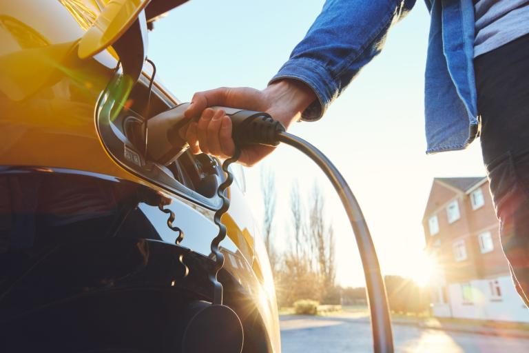 A close up shot of someone holding an electric vehicle charging plug in the back of a yellow car.