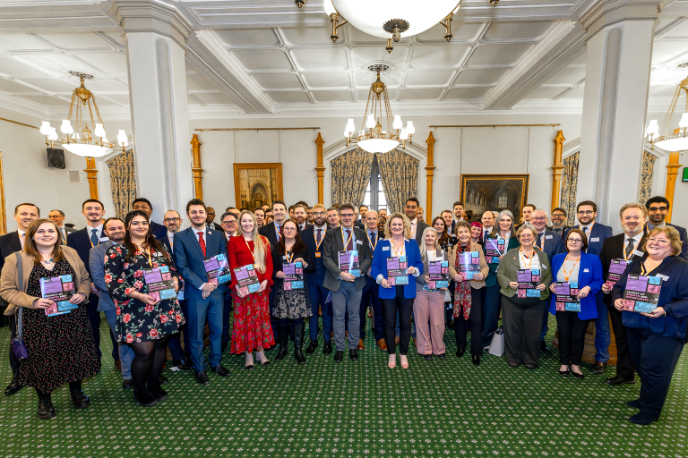 A large group of people inside a grand room standing in a semi-circle. 